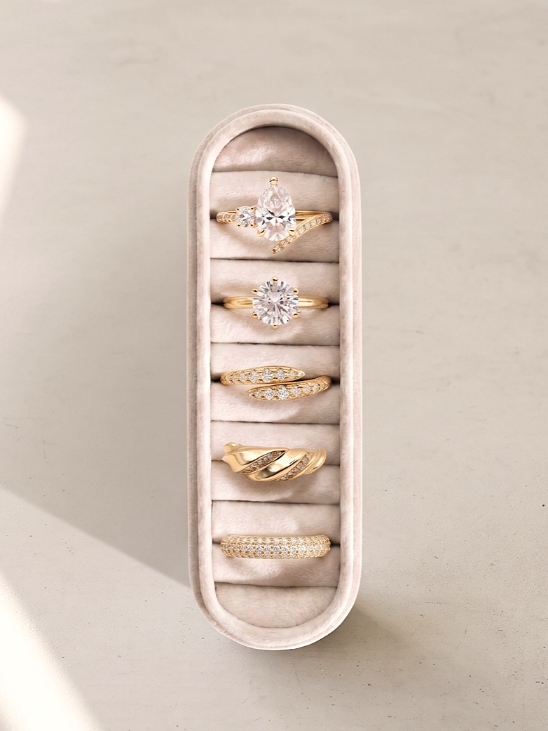 Five gold rings of varying designs are displayed in a vertical, rounded velvet jewelry organizer on a neutral beige surface.